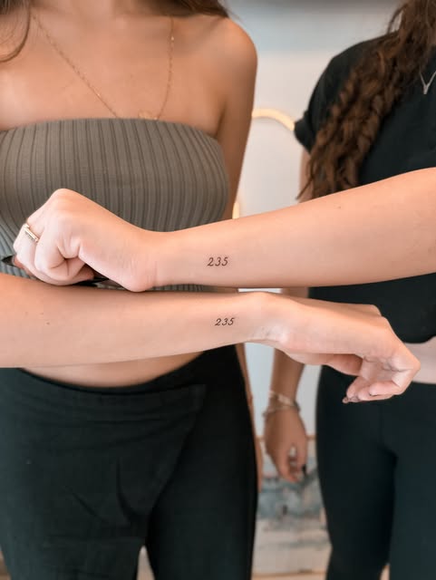 Duas pessoas com o mesmo número 235 tatuado em traço fino nos antebraços